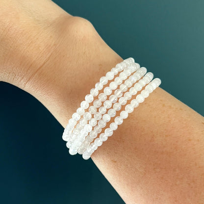 Stack of five white moonstone crystal bead bracelets on a woman's wrist against a teal background