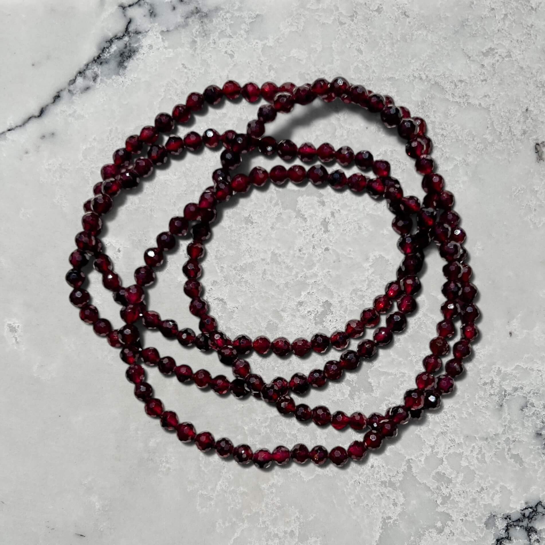 Stack of Faceted Garnet crystal bead bracelets on a white marble surface