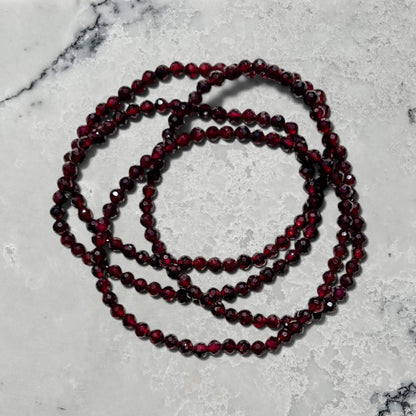 Stack of Faceted Garnet crystal bead bracelets on a white marble surface