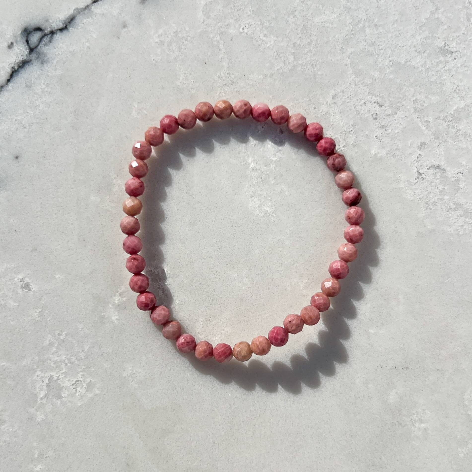 Pink Rhodonite faceted crystal bead bracelet on a light marble surface
