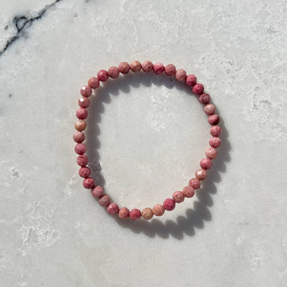 Pink Rhodonite faceted crystal bead bracelet on a light marble surface