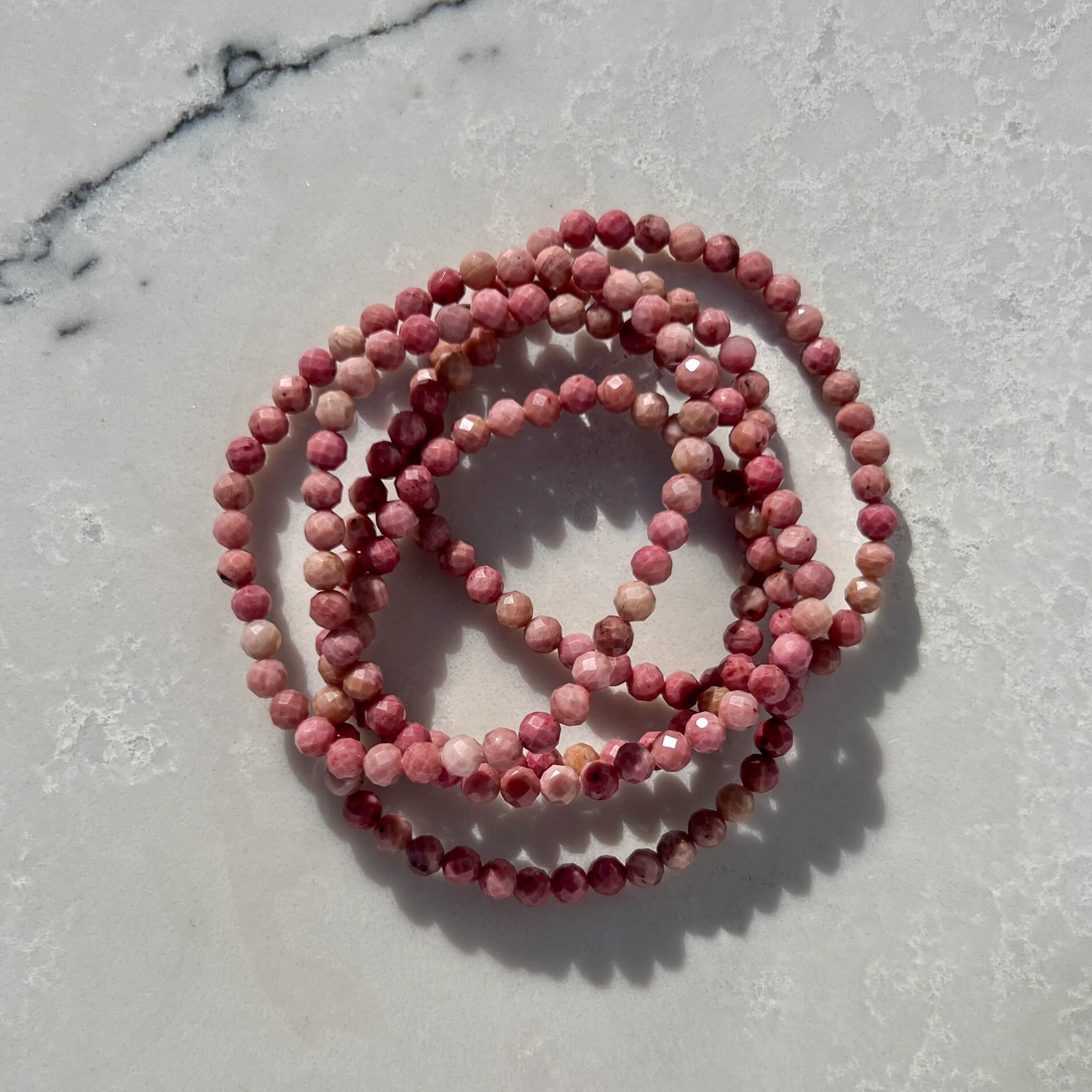 Pink Rhodonite faceted crystal bead bracelets on a light grey marble surface