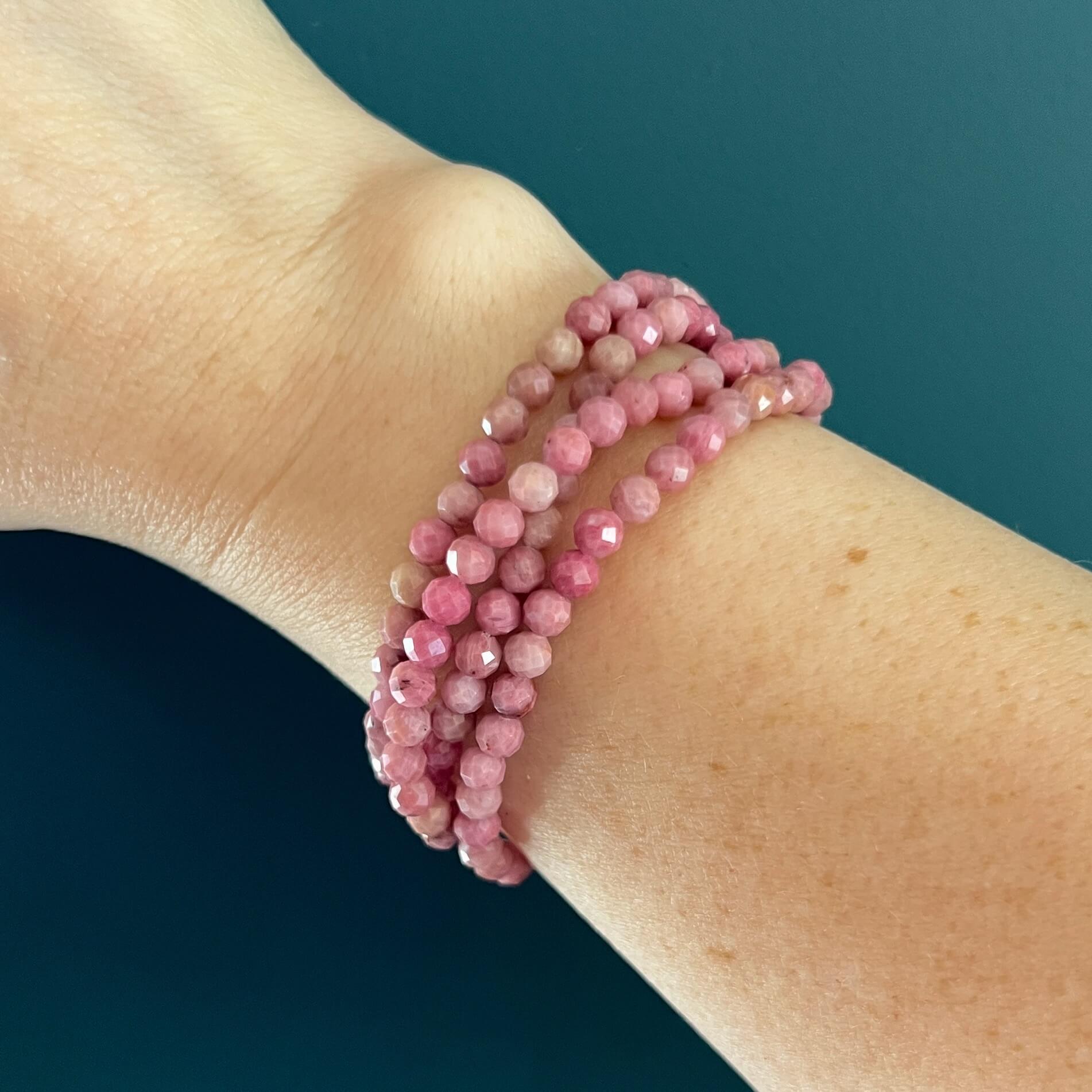 Pink Rhodonite faceted crystal bead bracelets on a woman's wrist against a eucalyptus green background