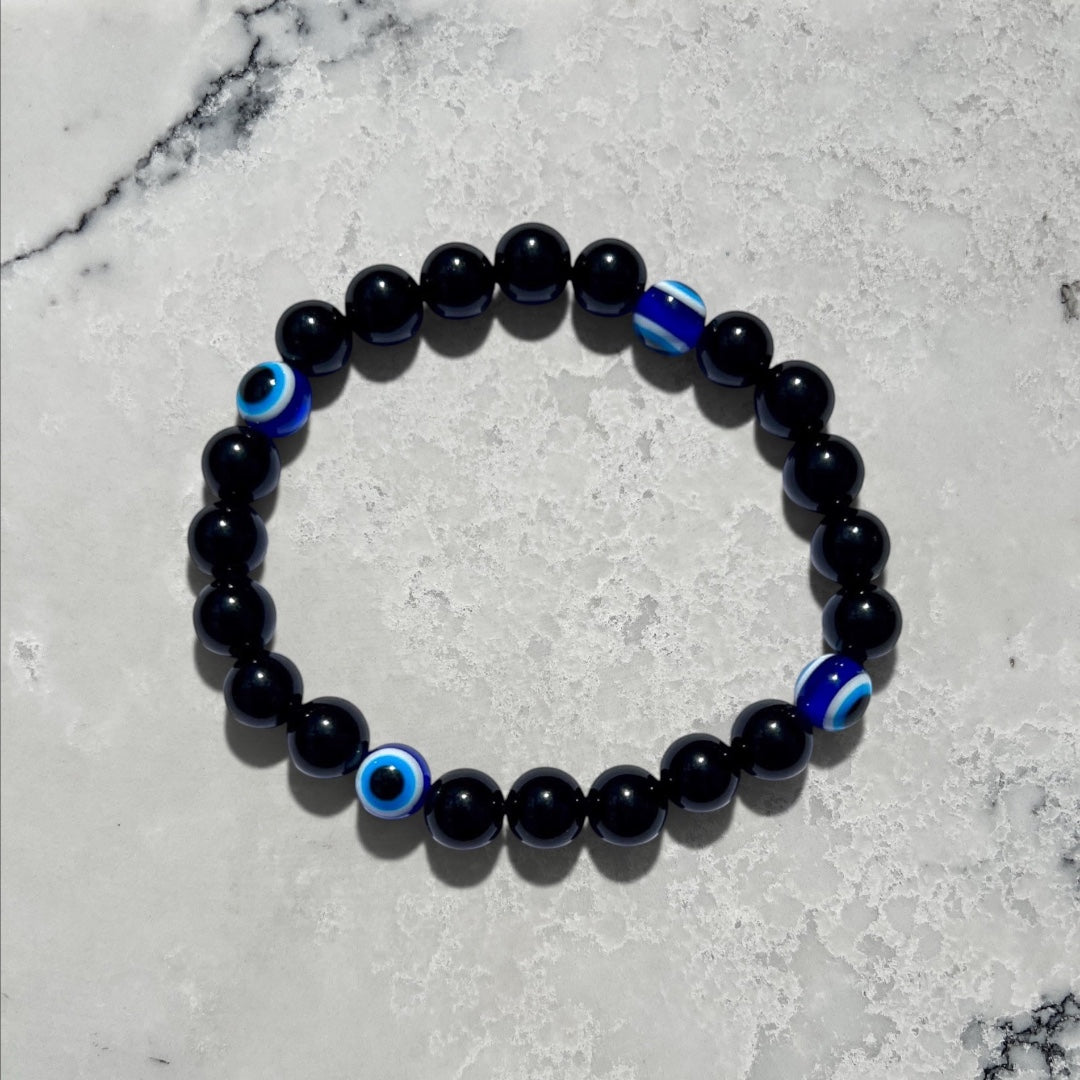 Rock + Realm Crystals black obsidian beaded bracelet with blue and white evil eye charms for protection and good luck against a natural marble surface