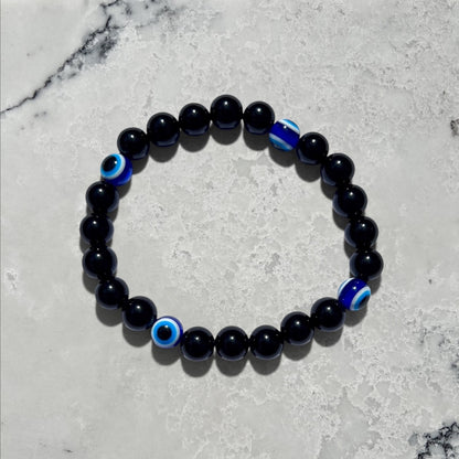 Rock + Realm Crystals black obsidian beaded bracelet with blue and white evil eye charms for protection and good luck against a natural marble surface