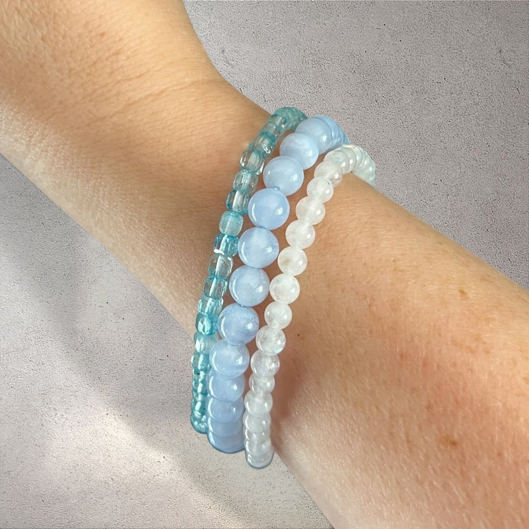 Rock + Realm Crystals stack of three beaded bracelets in shades of blue and white, featuring smooth blue topaz, blue lace agate and moonstone.
