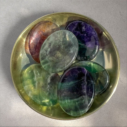 Rock + Realm Crystals polished oval fluorite worry stones in green, purple, and pink hues, displayed in a brass bowl.