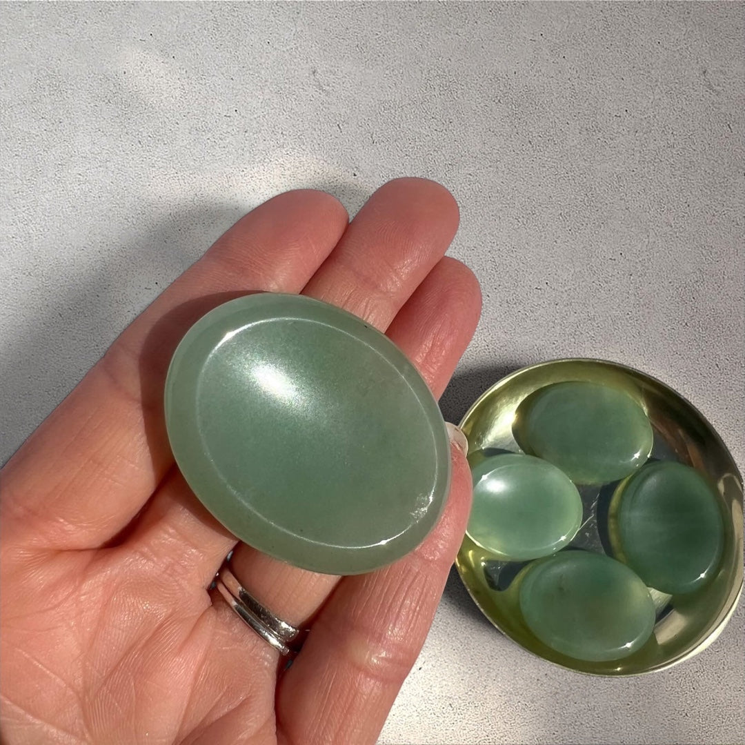 Smooth green aventurine worry stone held flat in hand, with more stones in a small dish.