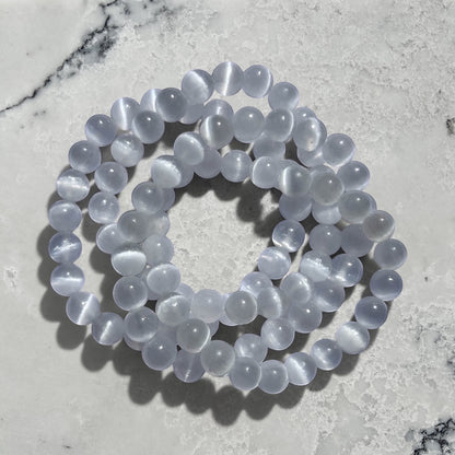 Stack of Rock + Realm Crystals large 8mm selenite crystal bead bracelets, white translucent beads with subtle chatoyancy shining in the sun on a marble surface