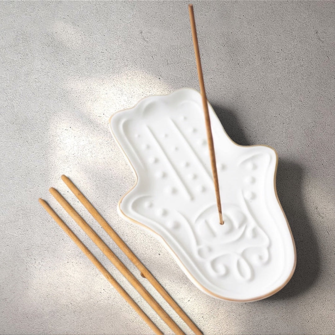 Rock + Realm Crystals white ceramic hamsa hand incense holder with gold trim, featuring embossed palm details and a central hole for incense sticks.