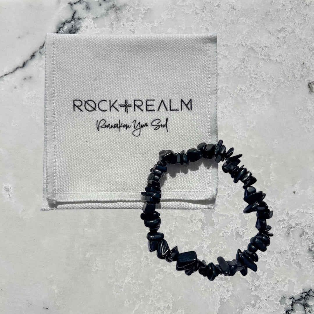 Rock + Realm black shungite chip bracelet with a white pouch featuring the brand logo.