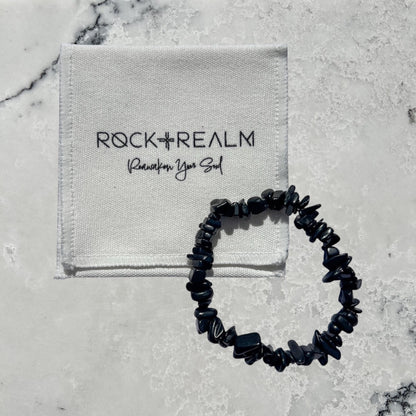 Rock + Realm black shungite chip bracelet with a white pouch featuring the brand logo.