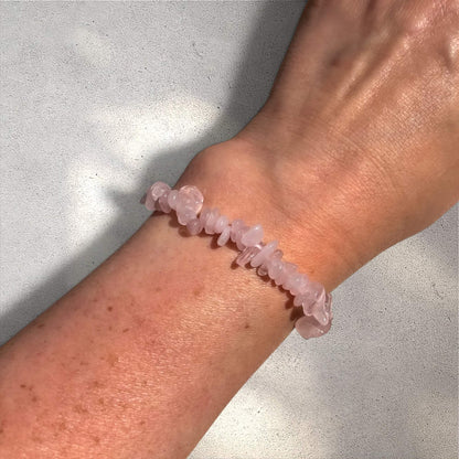 rose quartz crystal chip bracelet on a wrist against a neutral background
