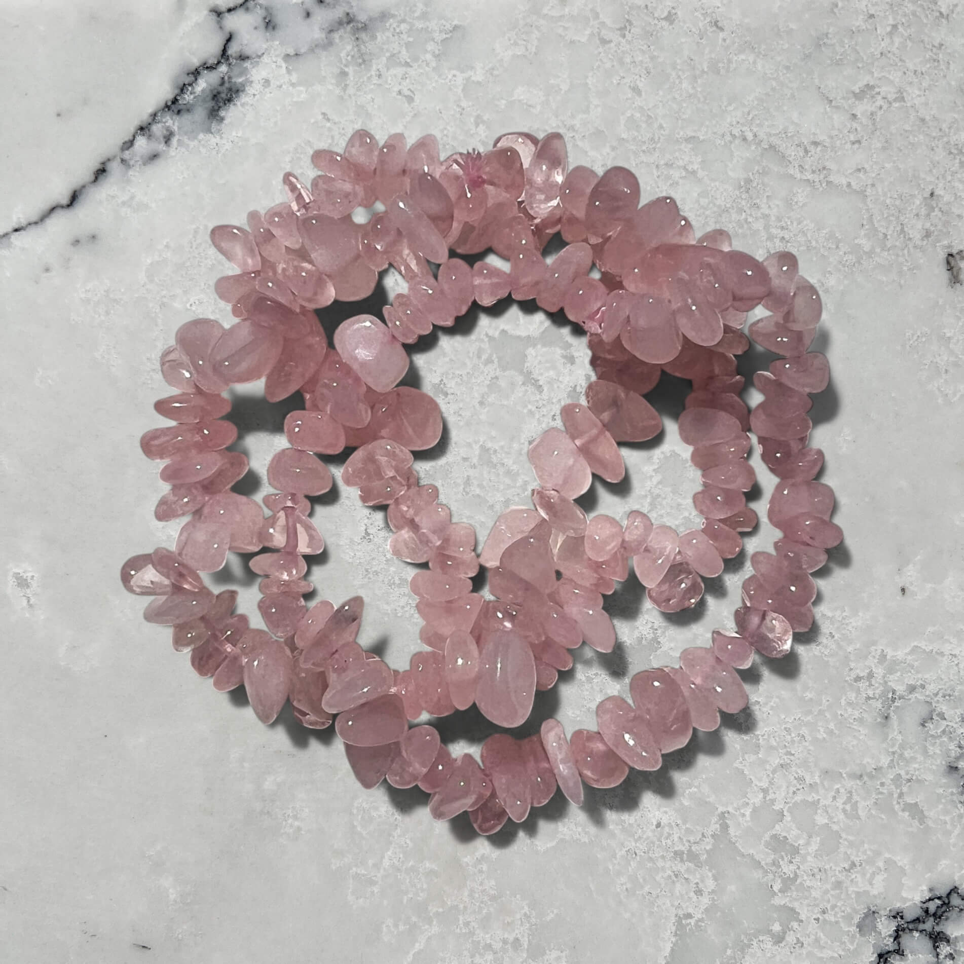 Stack of rose quartz crystal chip bracelets against a marble background