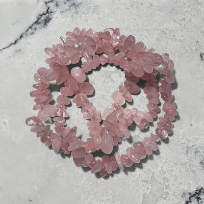Stack of rose quartz crystal chip bracelets against a marble background