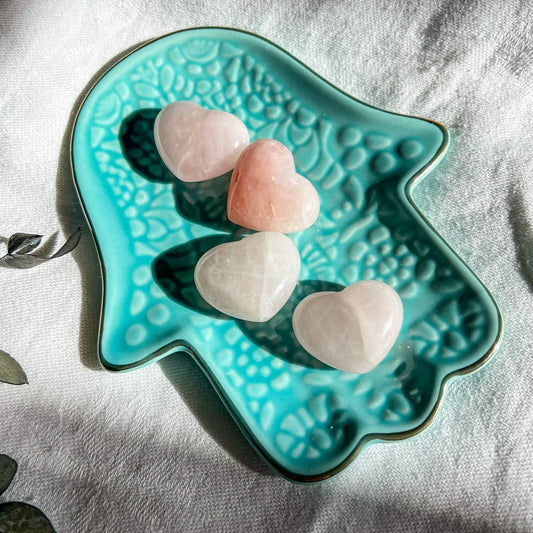 Pale pink rose quartz mini crystal hearts on a turquoise hamsa hand trinket dish
