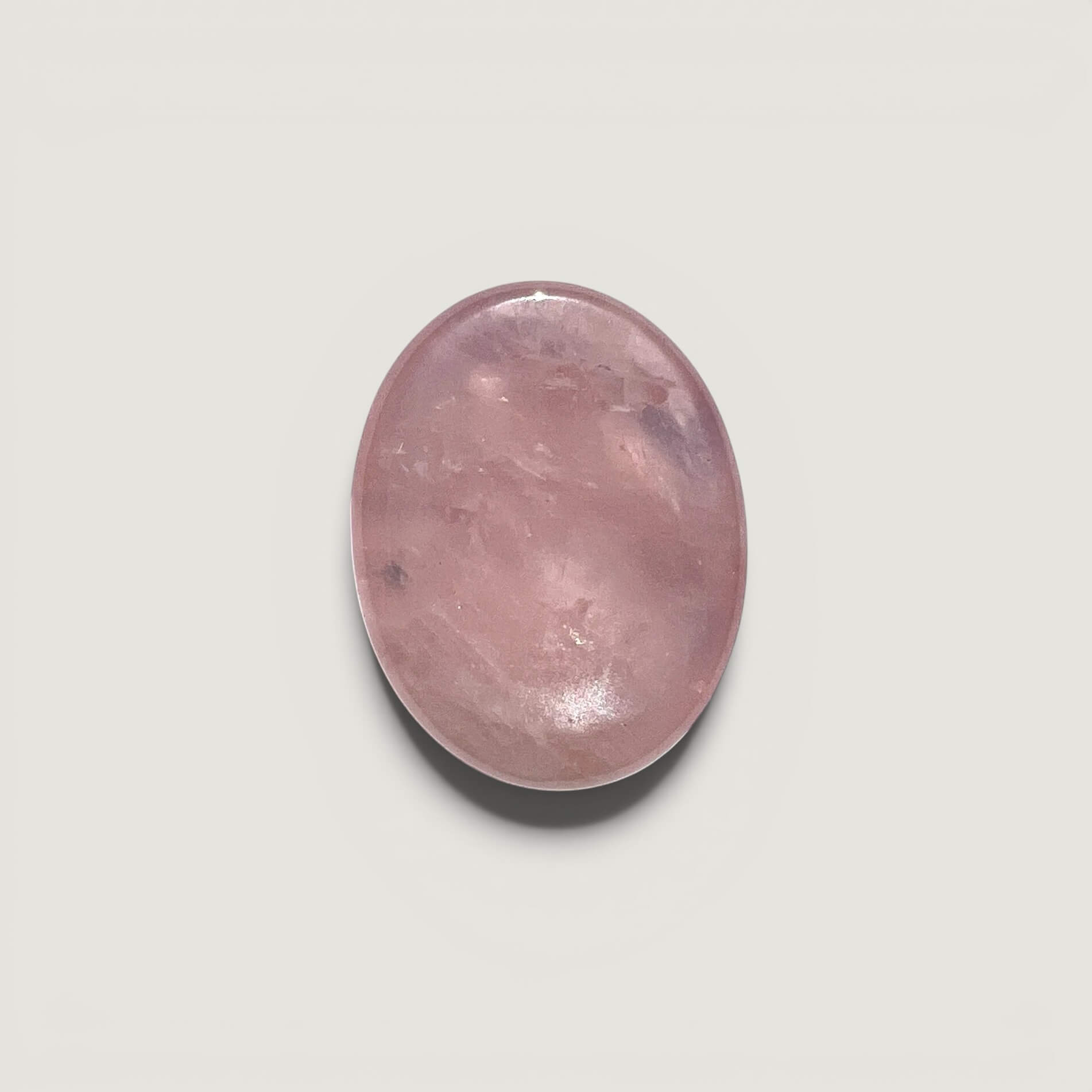A smooth, polished oval rose quartz worry stone in a soft pink hue, centred on a light grey background.