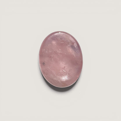 A smooth, polished oval rose quartz worry stone in a soft pink hue, centred on a light grey background.