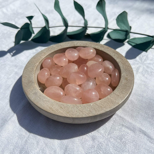 wooden bowl filled with gemmy pink rose quartz crystal tumblestones with a eucalyptus sprig in the background