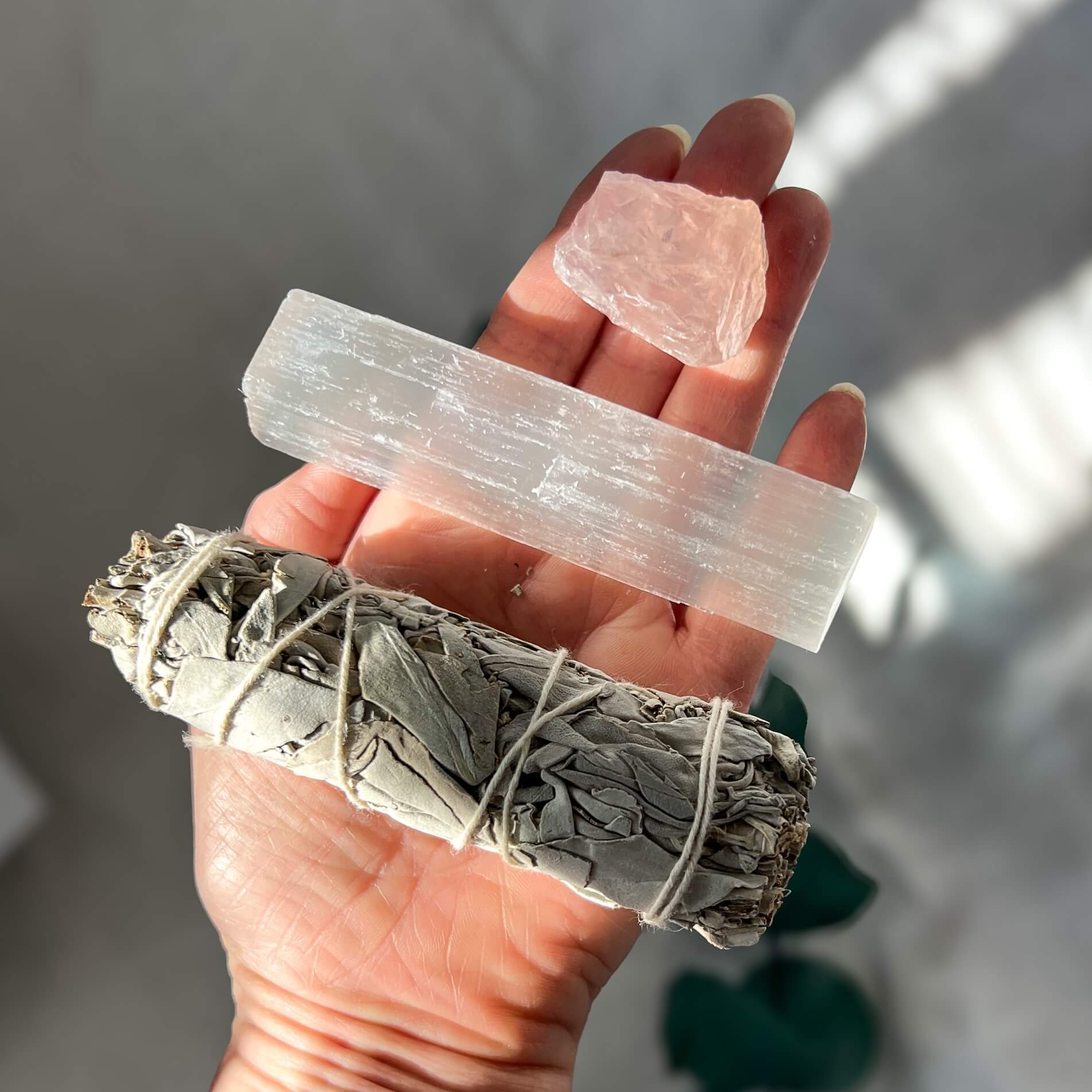 Sage, selenite and rose quartz crystal laid out on an open hand held to camera