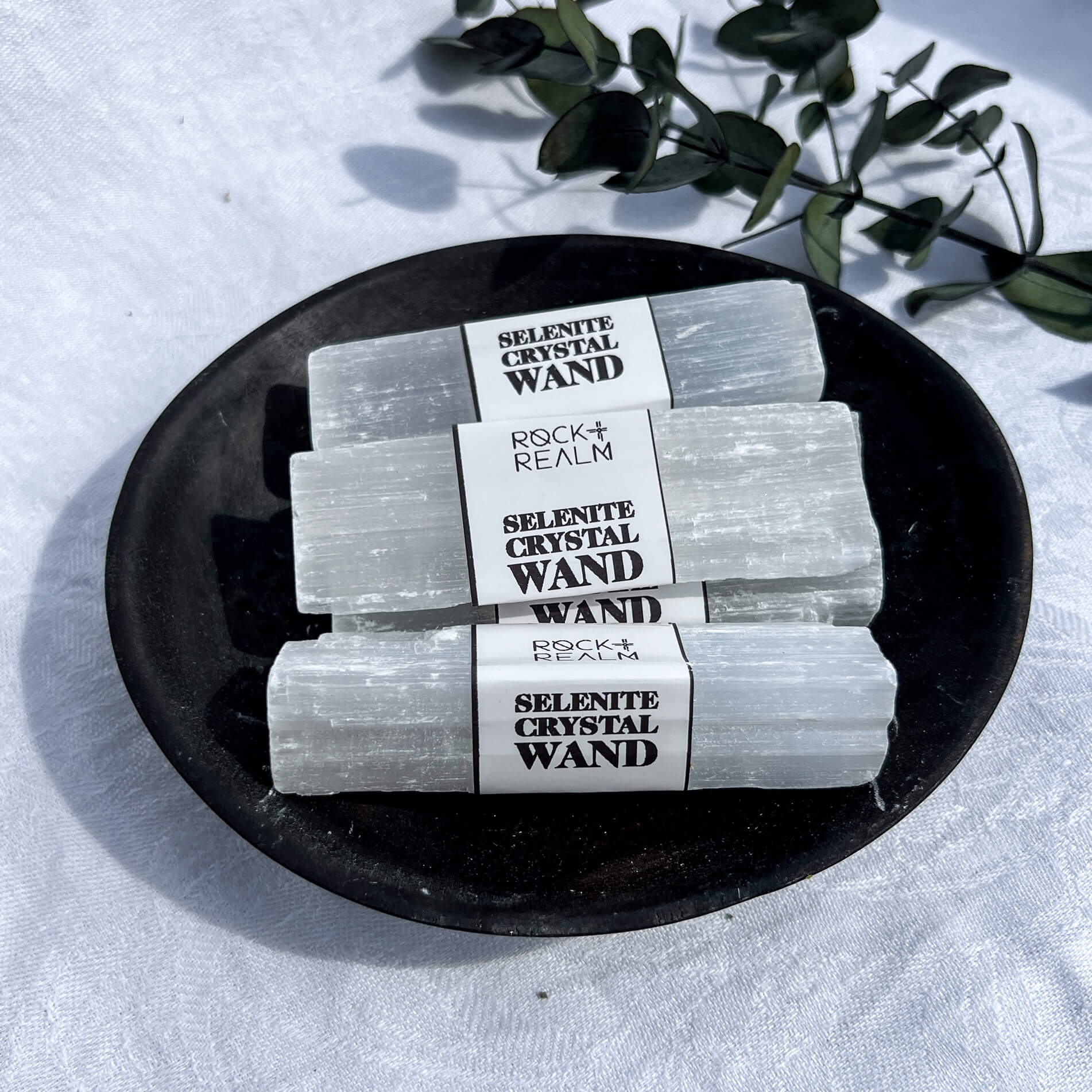 A bundle of white Selenite Crystal Wands grouped in a black wooden dish