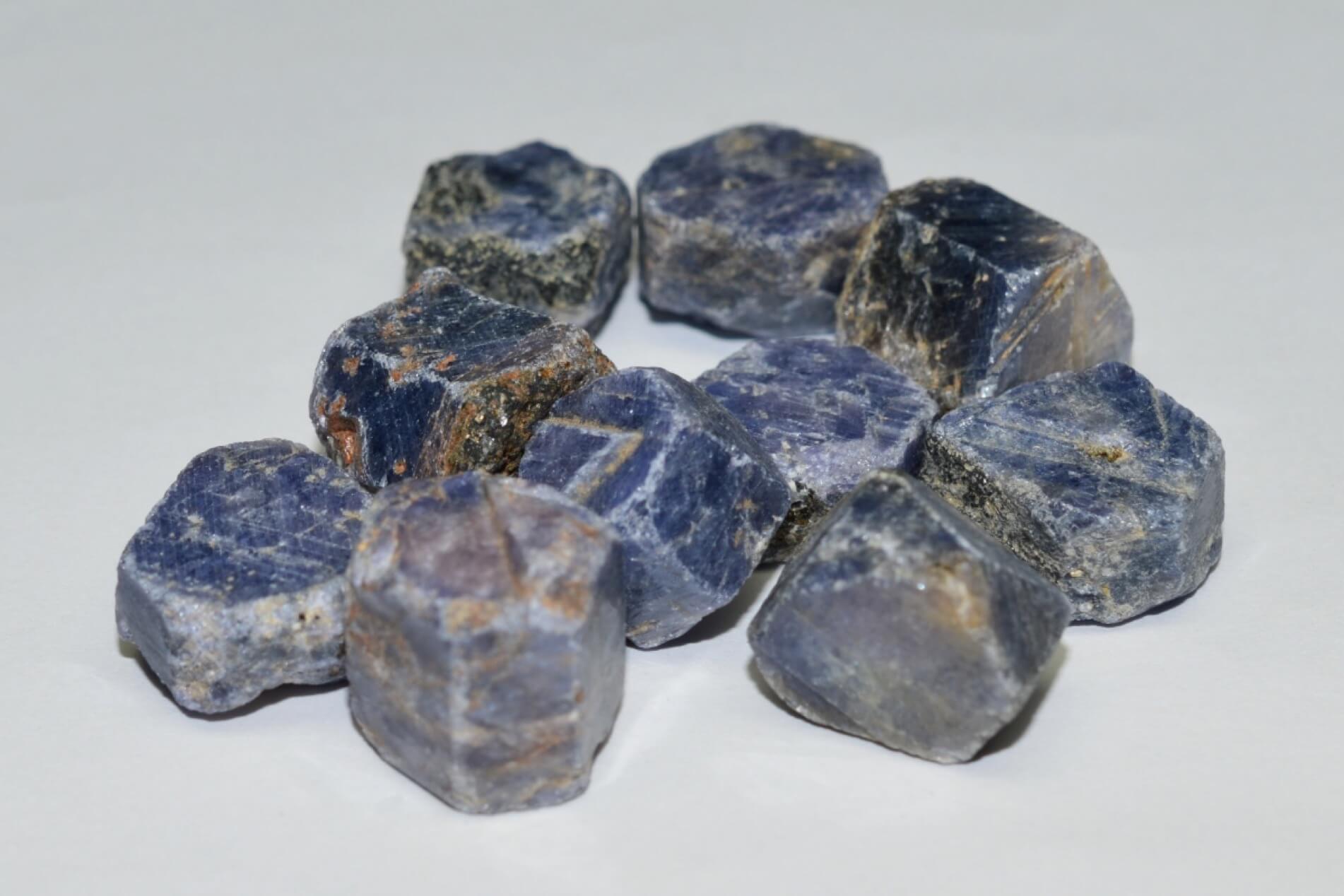 A pile of raw blue sapphire gemstone chunks arranged on a plain white background. 