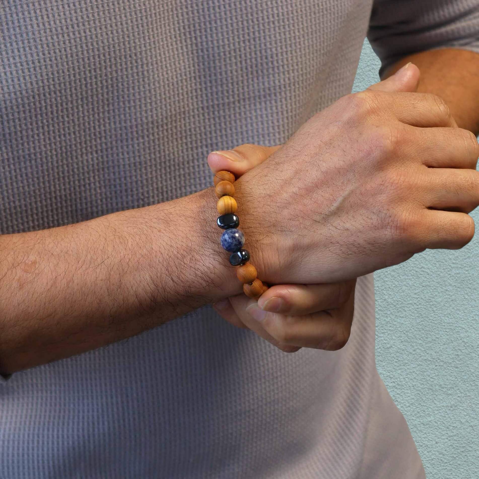 Man wearing a cedar wood and sodalite bead bracelet against a pale green background