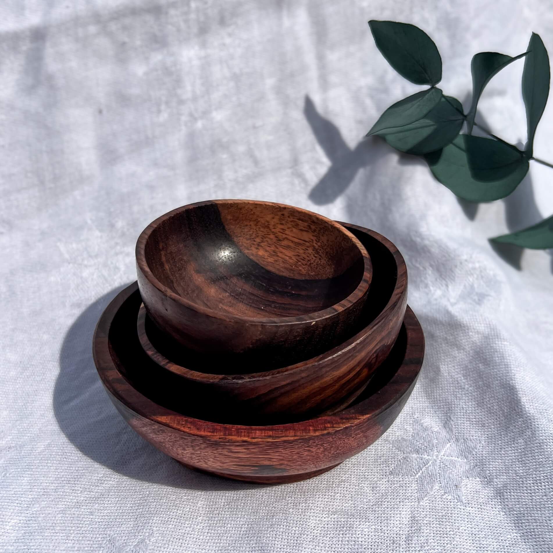 Stack of Indian Rose Wood bowls on a light fabric background with green leaves.