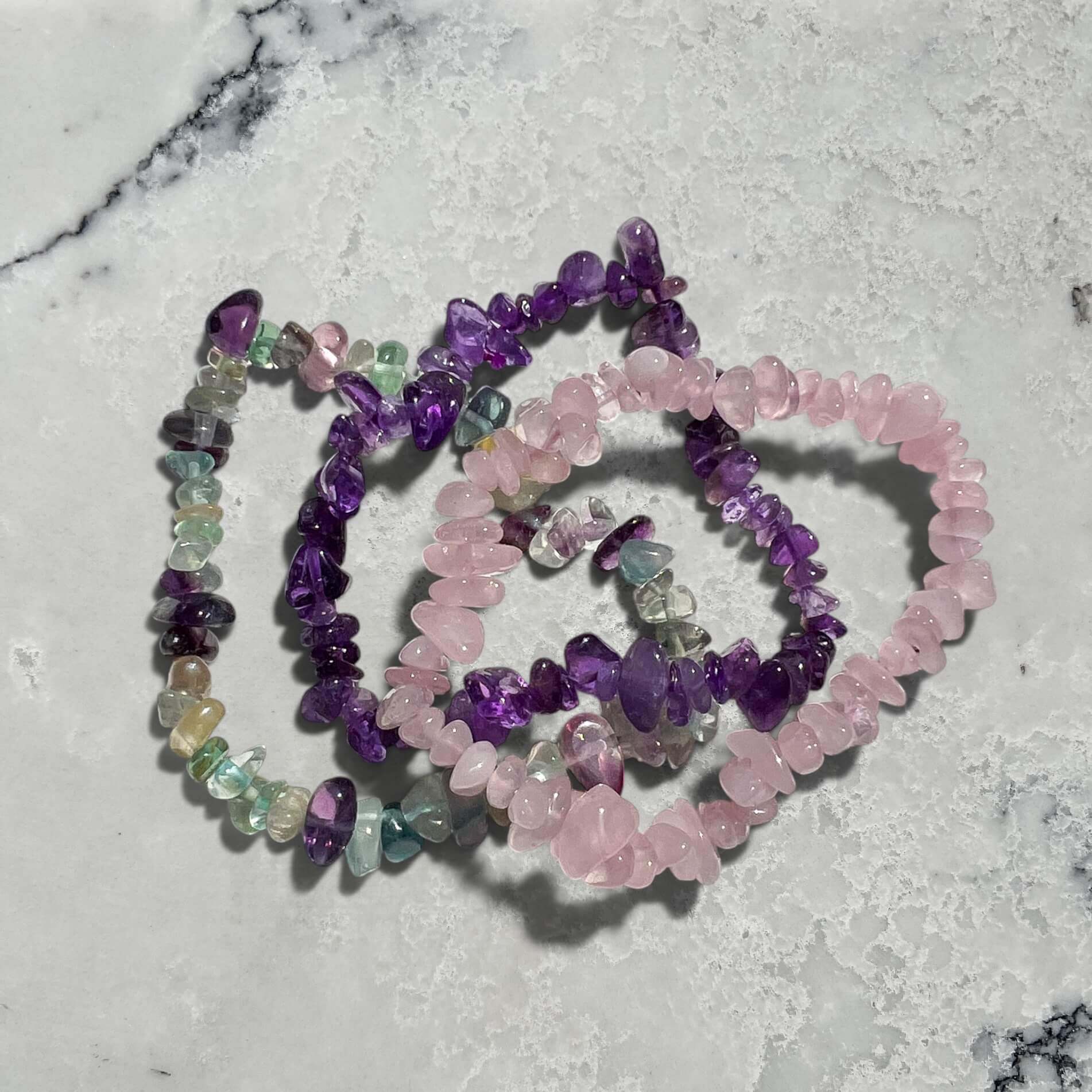 Stack of three purple and pink crystal chip bracelets made of fluorite, amethyst and rose quartz on a marble surface