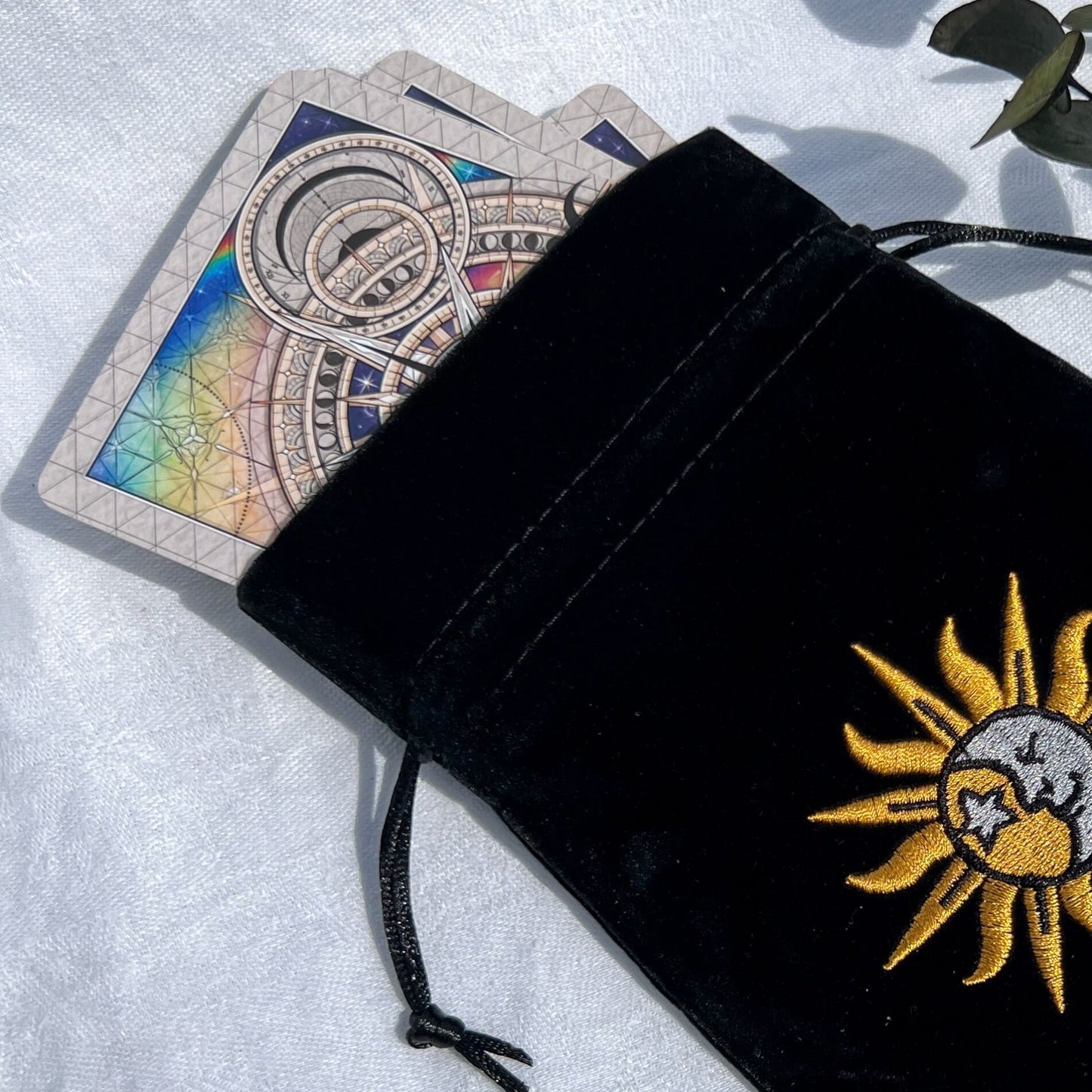 Black velvet celestial oracle card bag with an embroidered sun and moon emblem with oracle cards poking out
