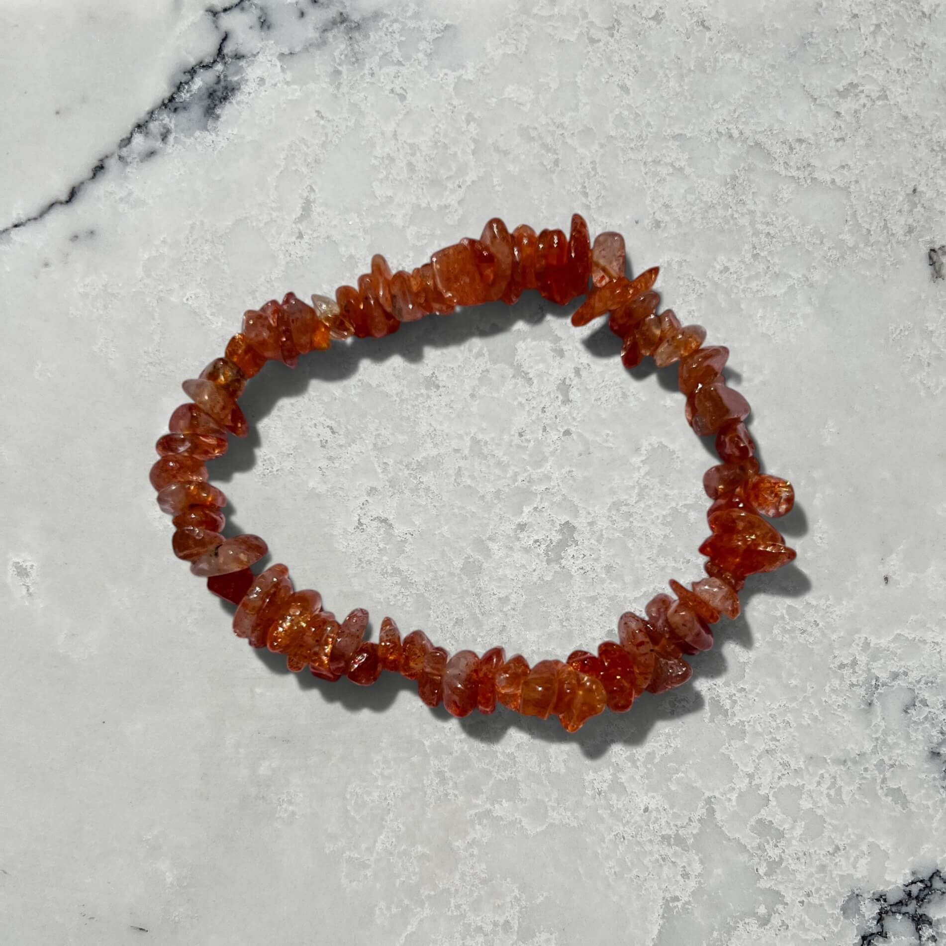 Orange high grade sunstone crystal chip bracelet with sparkle on a grey marble surface