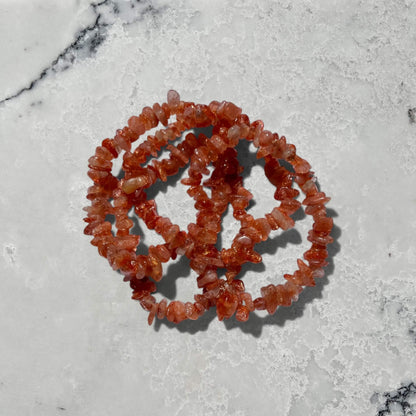 Stack of Orange high grade sunstone crystal chip bracelets with sparkle on a grey marble surface
