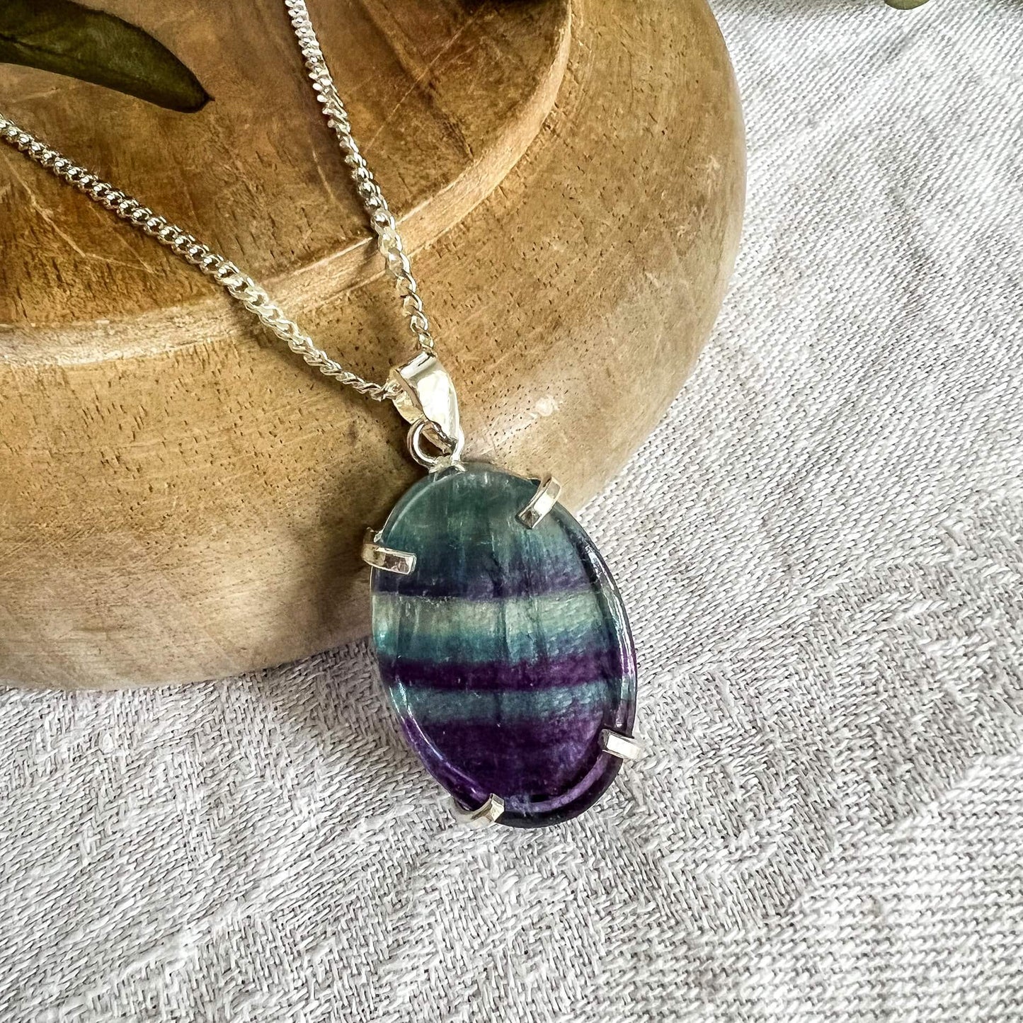 Pale aqua blue and purple striped fluorite crystal pendant on a silver chain close up