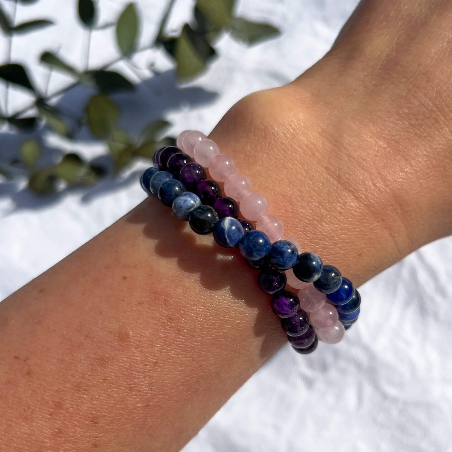 A woman's wrist wearing three healing crystal bead bracelets in amethyst, rose quartz & sodalite