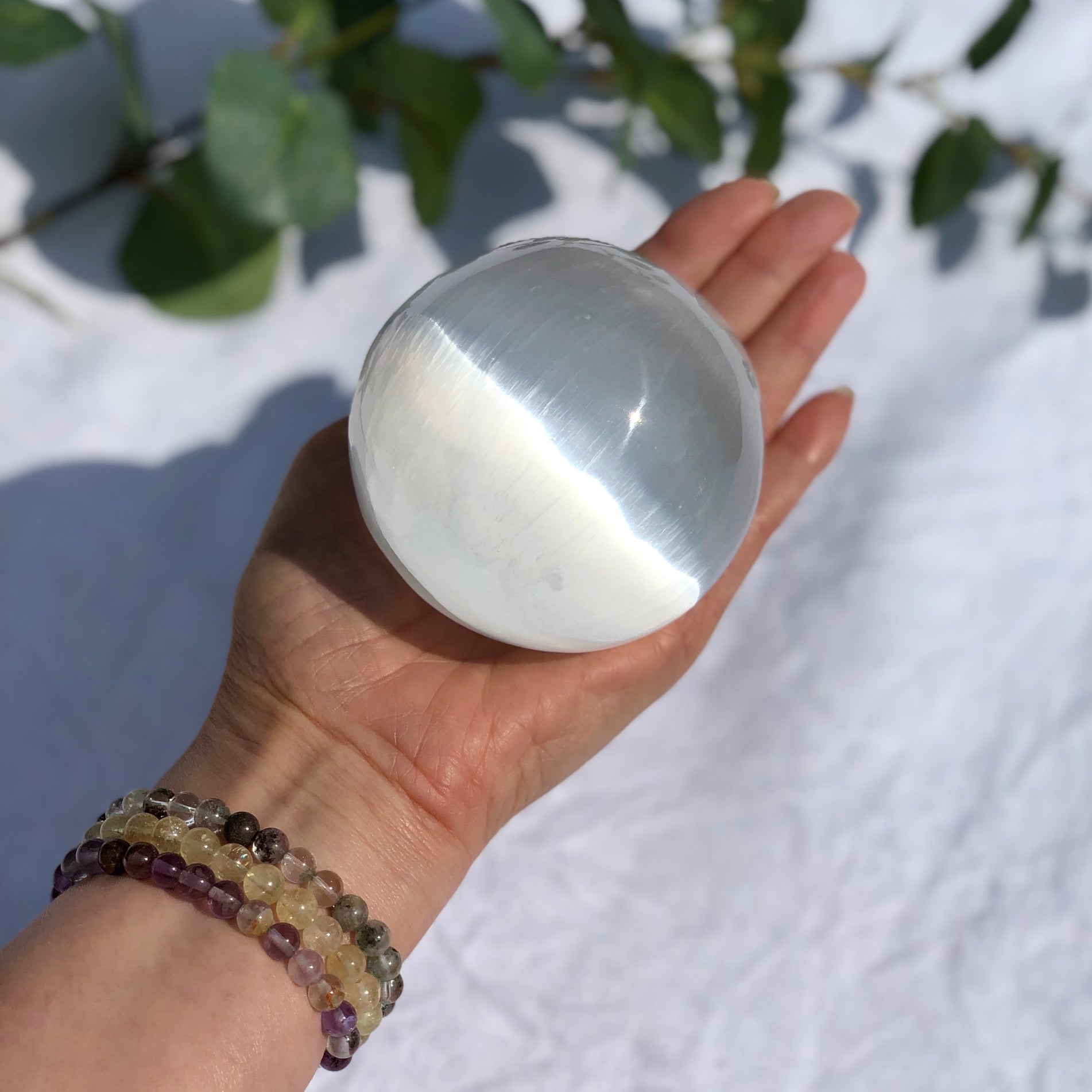 Extra large white and shiny selenite crystal sphere held in an open palm
