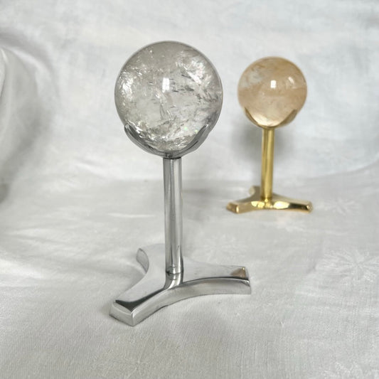Tall aluminium crystal display stand with a quartz crystal sphere . A brass sphere holder and crystal ball in the background.