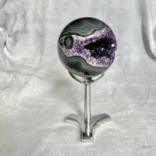 A beautiful dark purple amethyst geode sphere in a small crystal sphere holder display stand