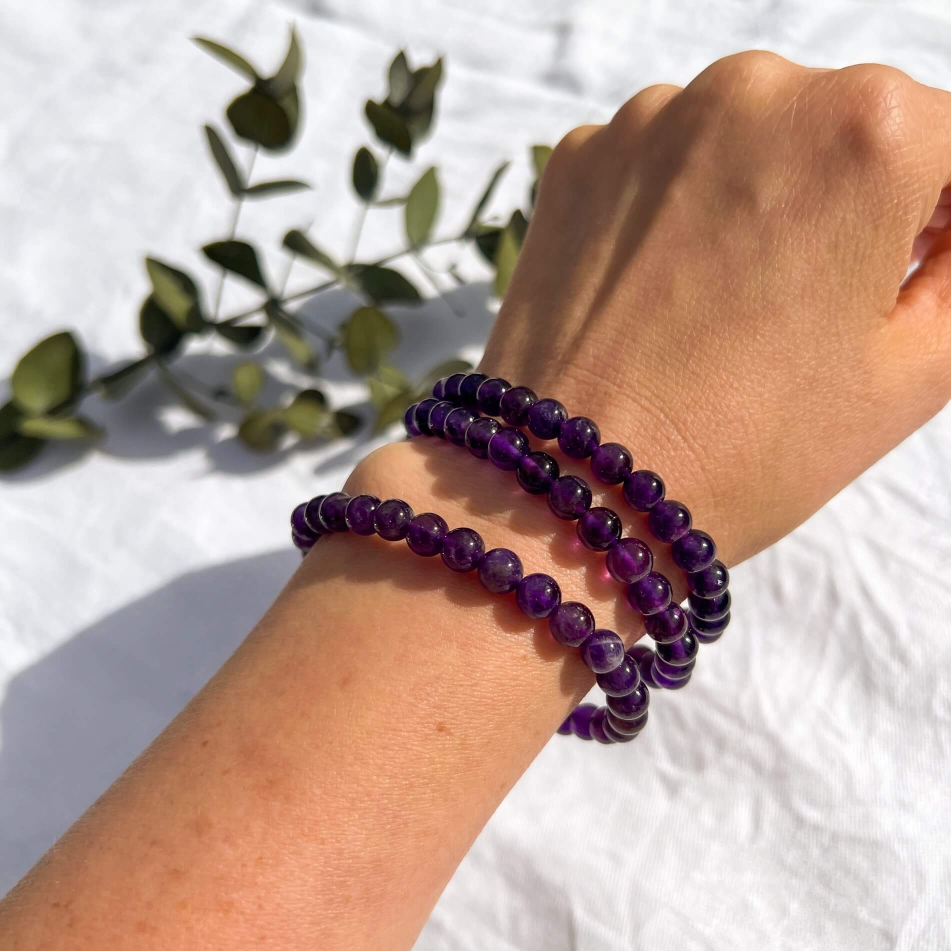 A woman's arm with three bright purple amethyst crystal bead bracelets