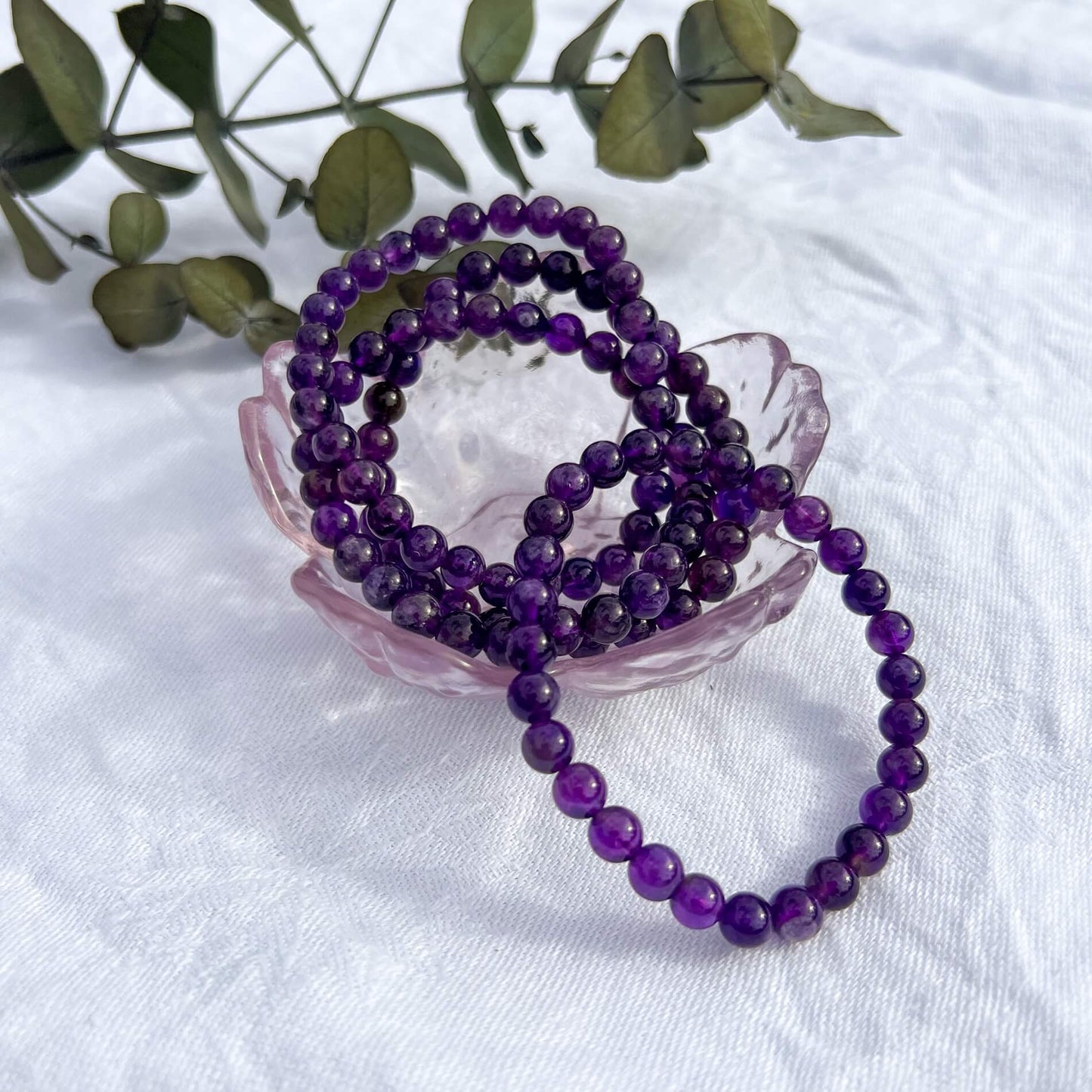 A pink glass dish full of bright purple amethyst crystal bead bracelets