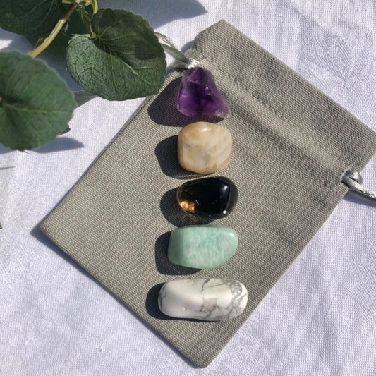 balance and tranquility healing crystal collection with white Howlite, green amazonite, smoky quartz, peach moonstone and purple amethyst tumble stones on a grey cotton gift bag