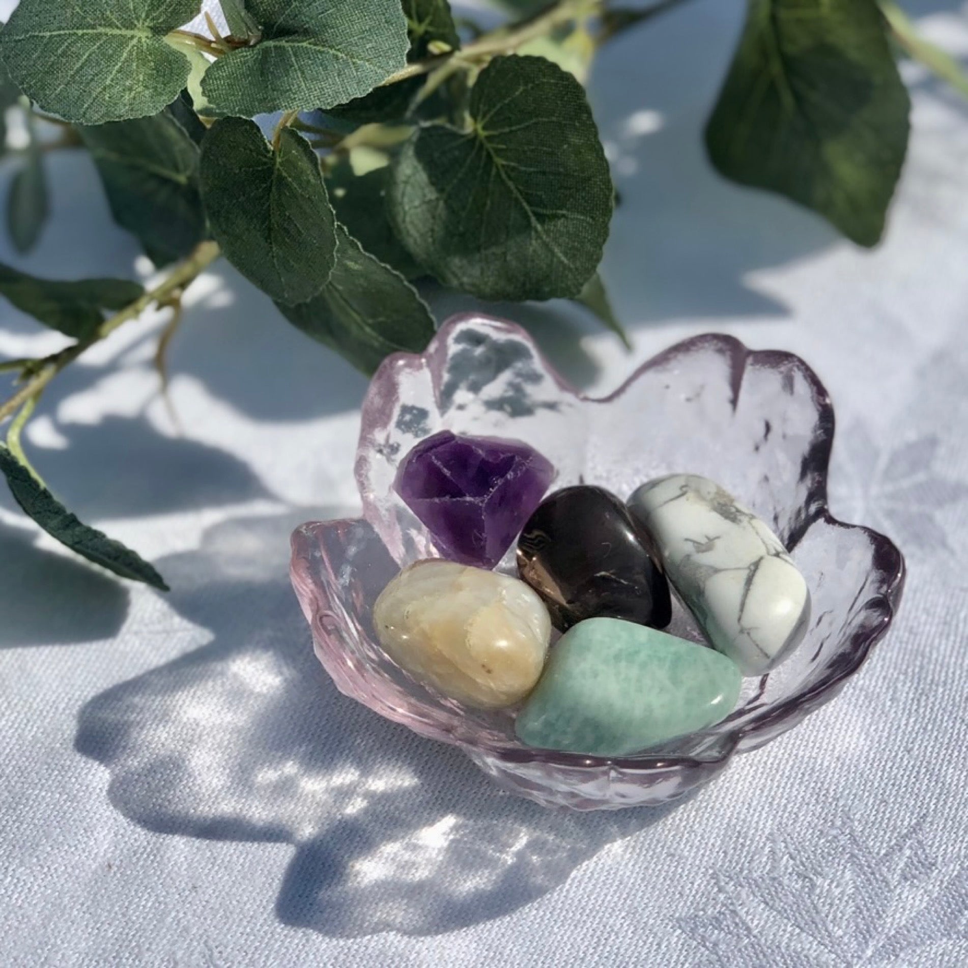 balance and tranquility healing crystal collection with white Howlite, green amazonite, smoky quartz, peach moonstone and purple amethyst tumble stones in a pink glass dish