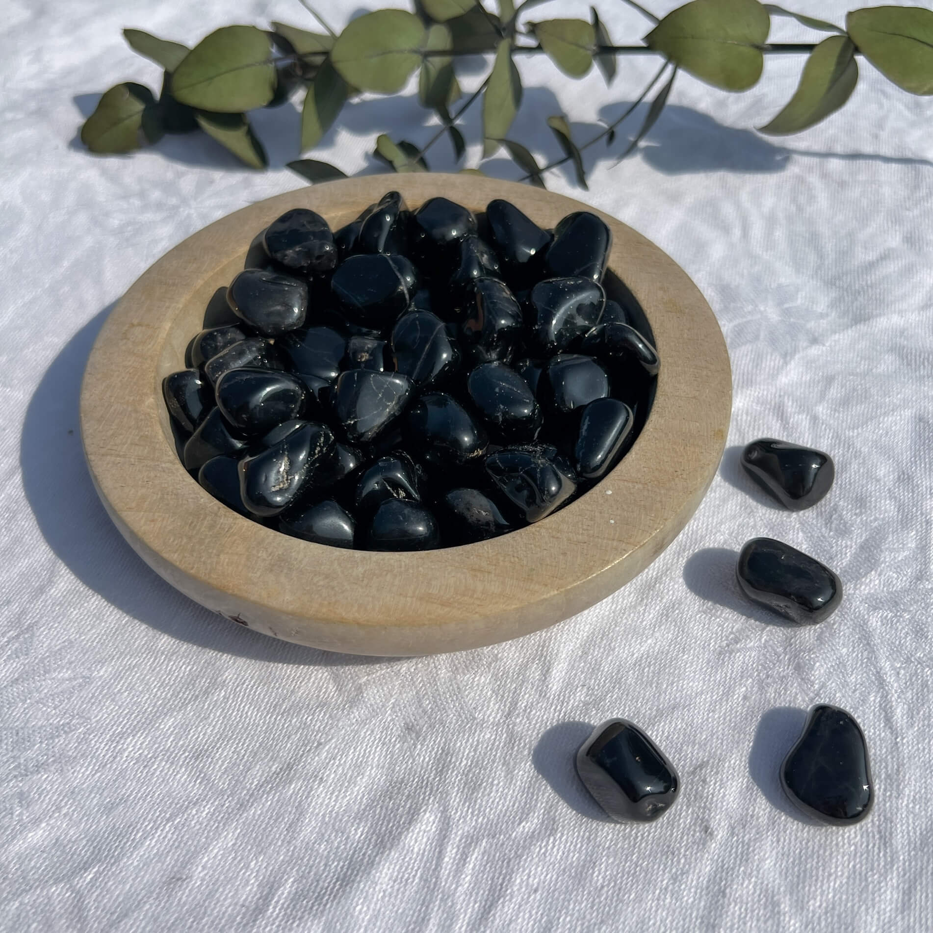 Wooden dish overflowing with small black tourmaline crystal tumblestones