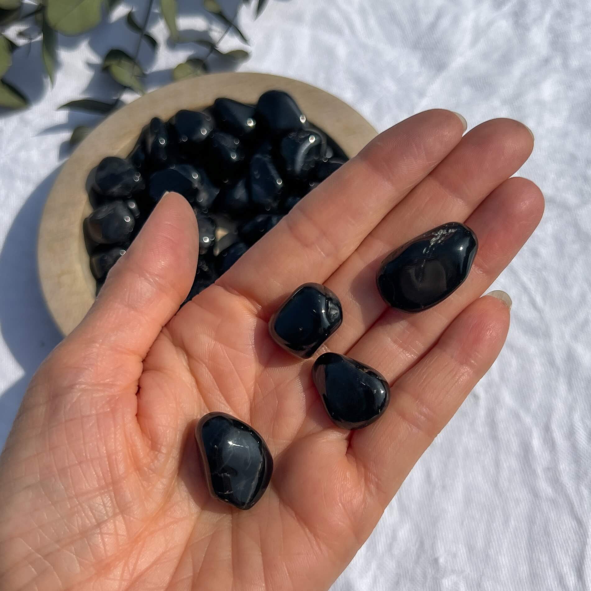 An open palm holding small black tourmaline crystal tumblestones