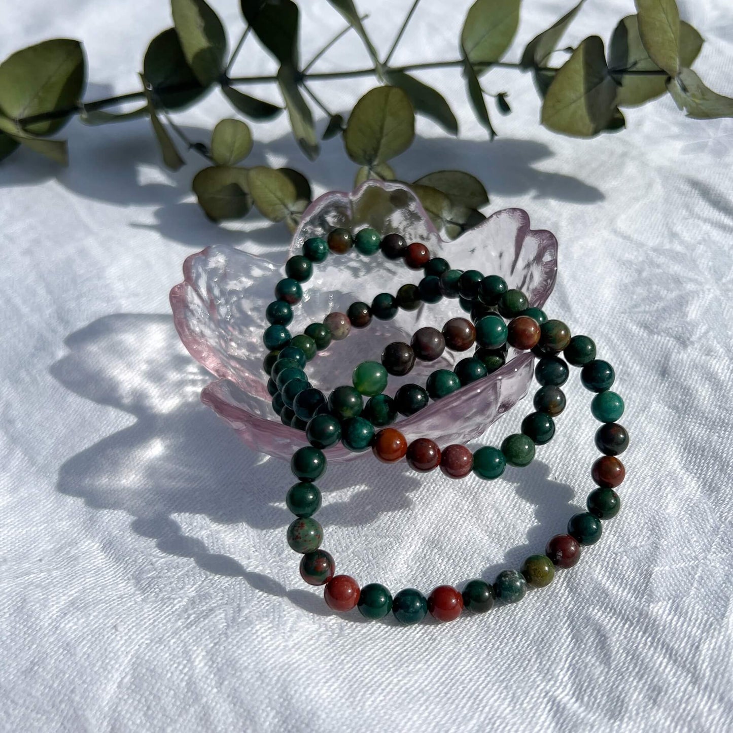A glass trinket dish filled with green & red Bloodstone crystal bead bracelets