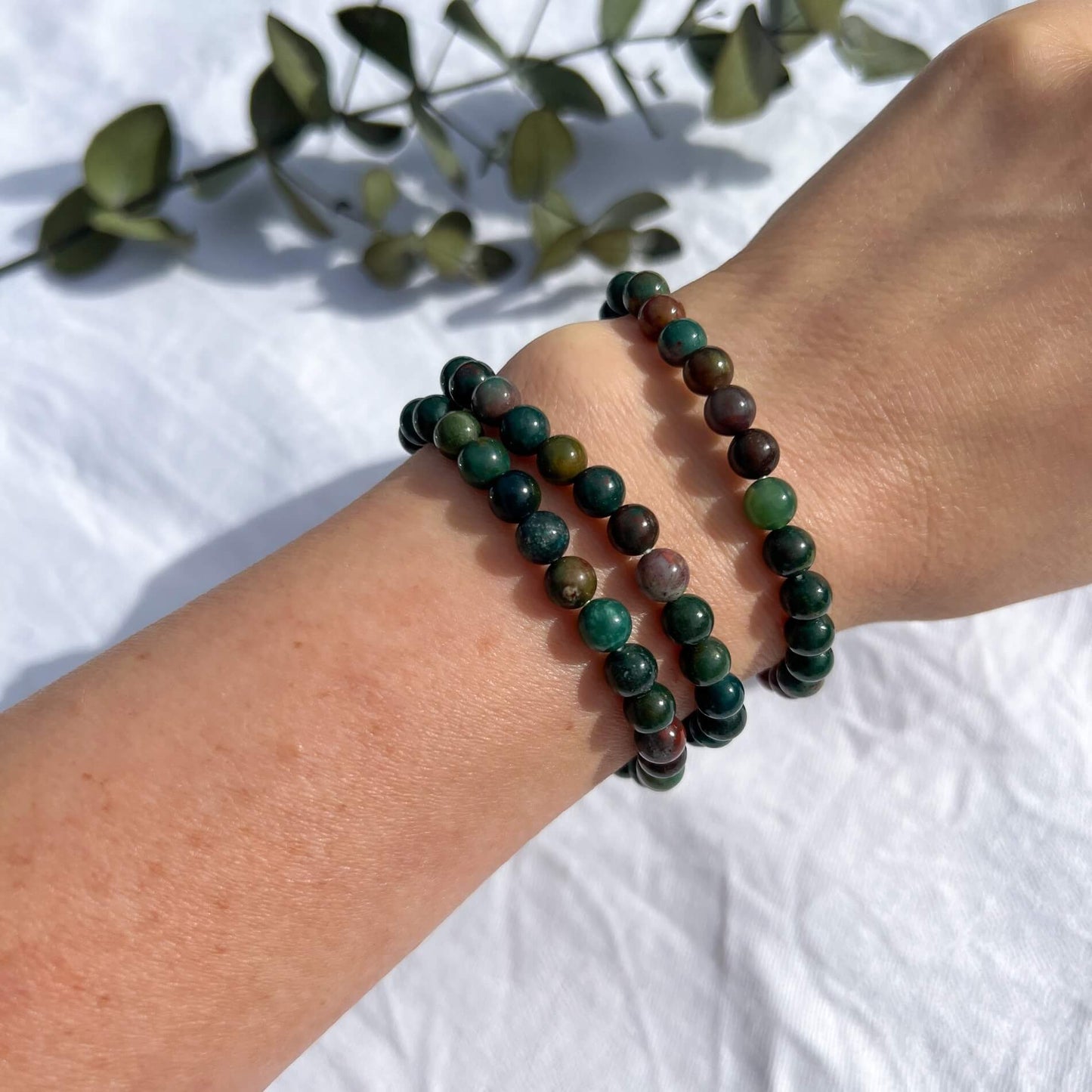 A woman's arm wearing three green & red Bloodstone healing crystal bead bracelets