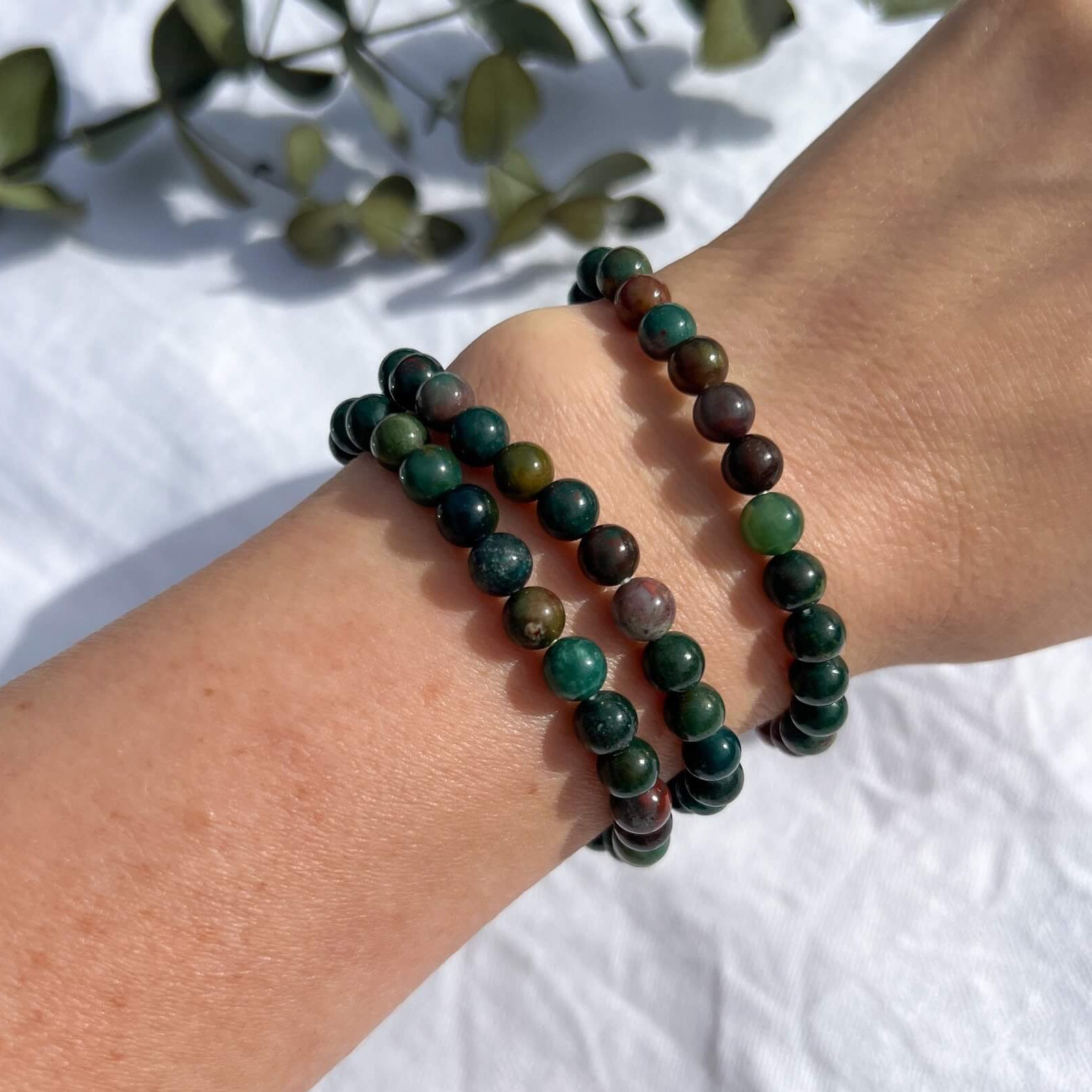 A woman's arm wearing three green & red Bloodstone healing crystal bead bracelets