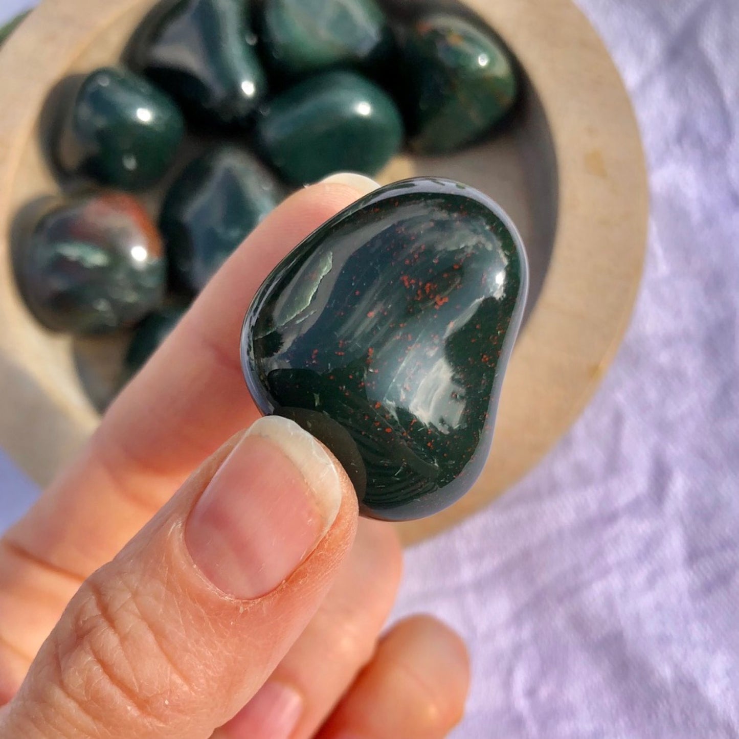 Glossy dark green and red flecked bloodstone pebble held to camera