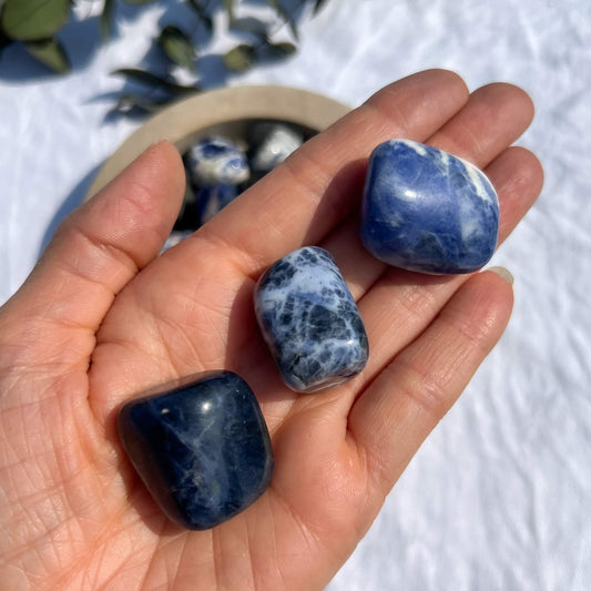 An open hand displaying three extra large blue and white sodalite crystal tumblestones