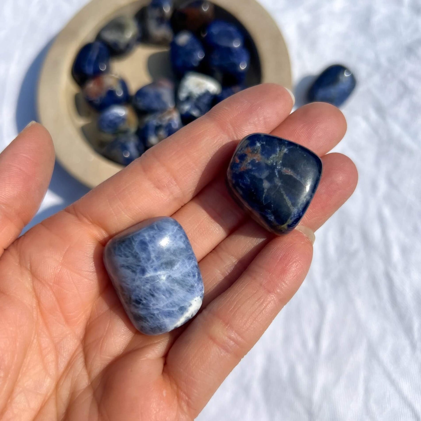 An open hand holding two blue and white large sodalite crystal tumblestones
