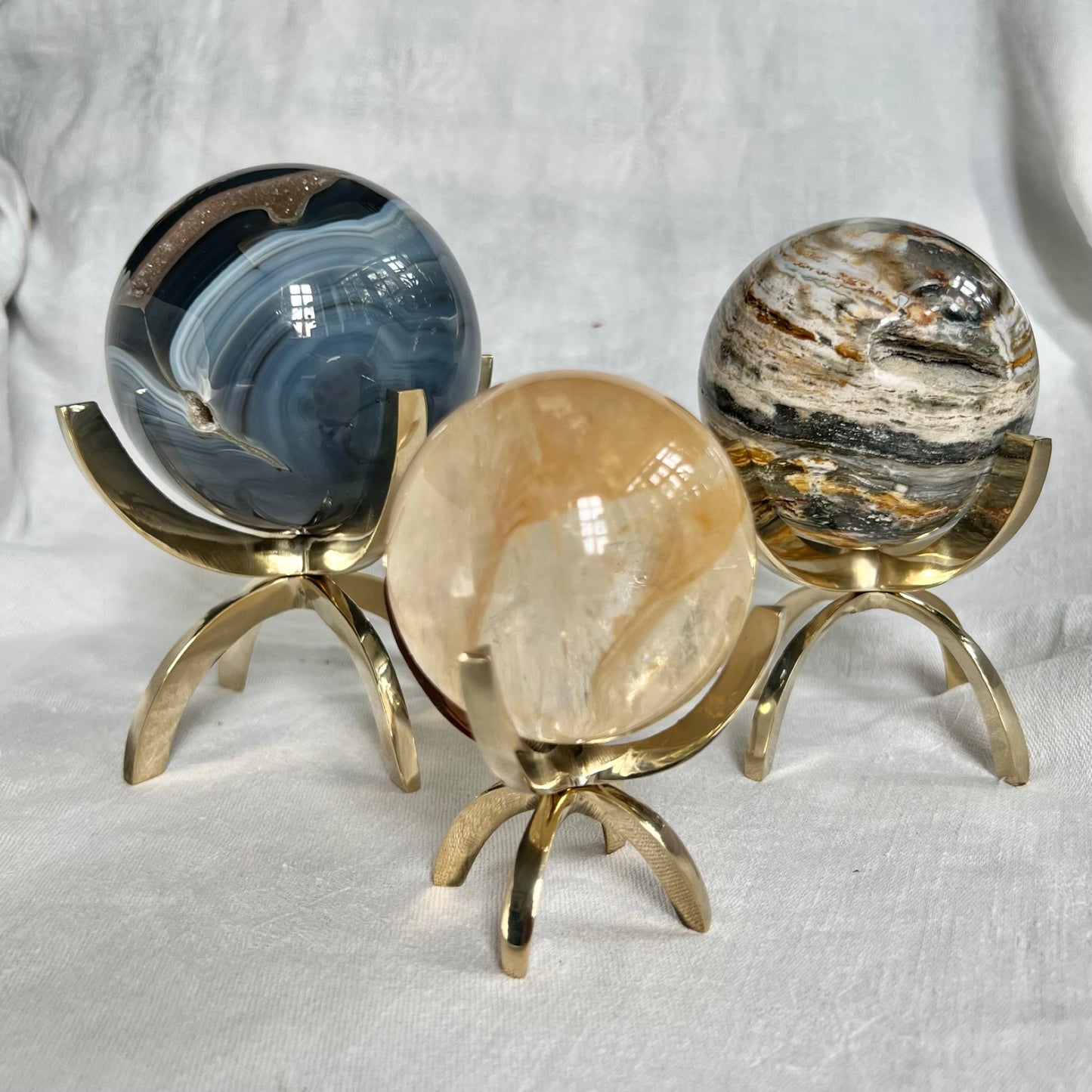 Three crystal spheres of different sizes displayed in shiny brass claw stands as a size comparison
